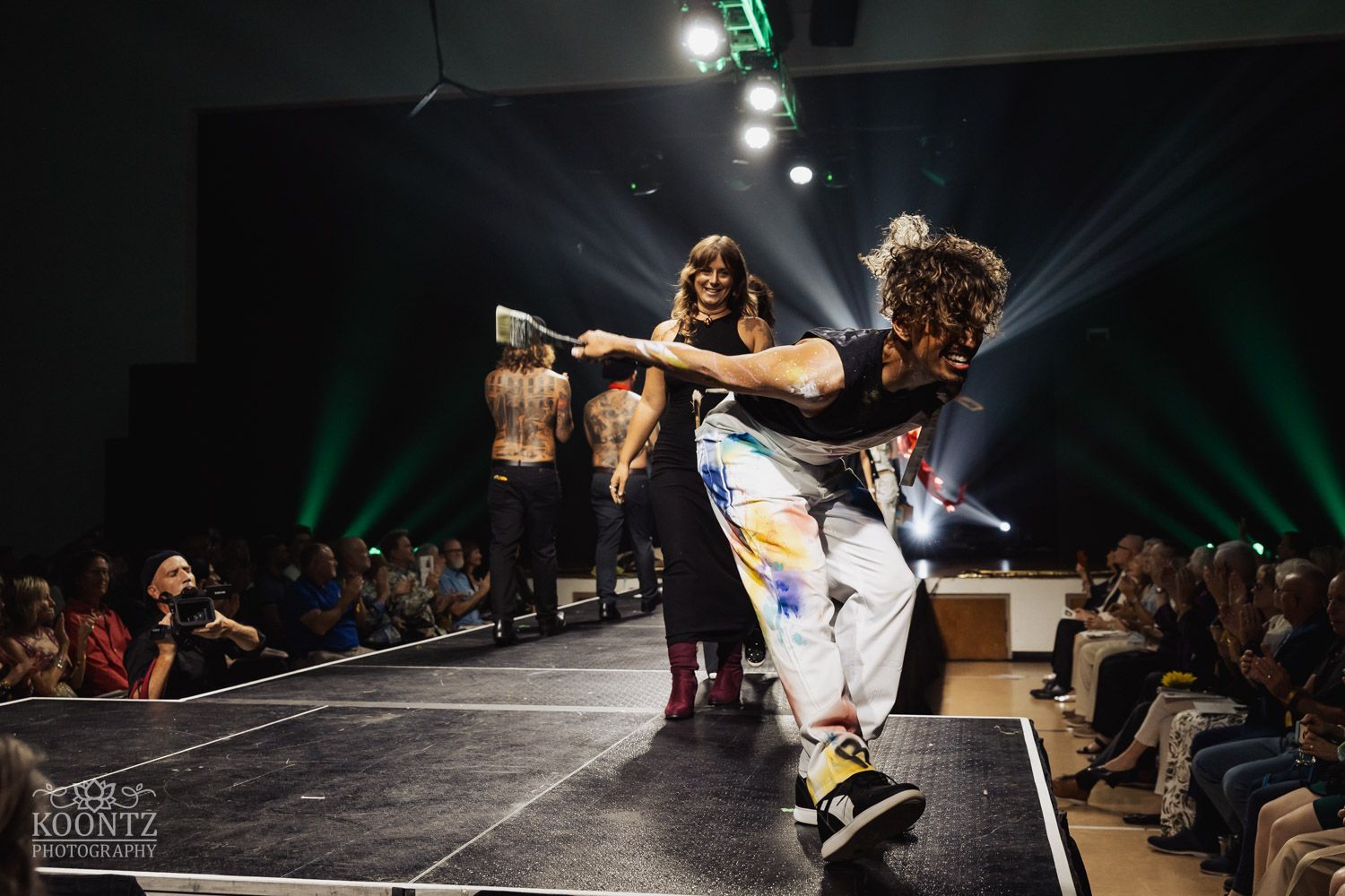 Dynamic performance on stage shows model in elaborate costume making dramatic movements under theatrical lighting.