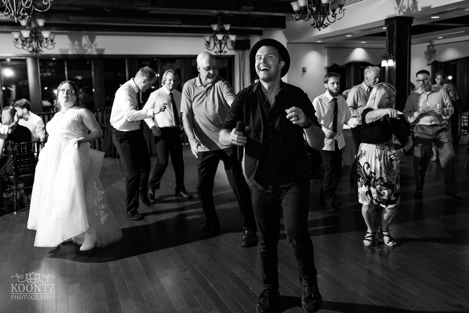 Wedding guests excitedly dance and celebrate on a crowded reception dance floor in black and white.