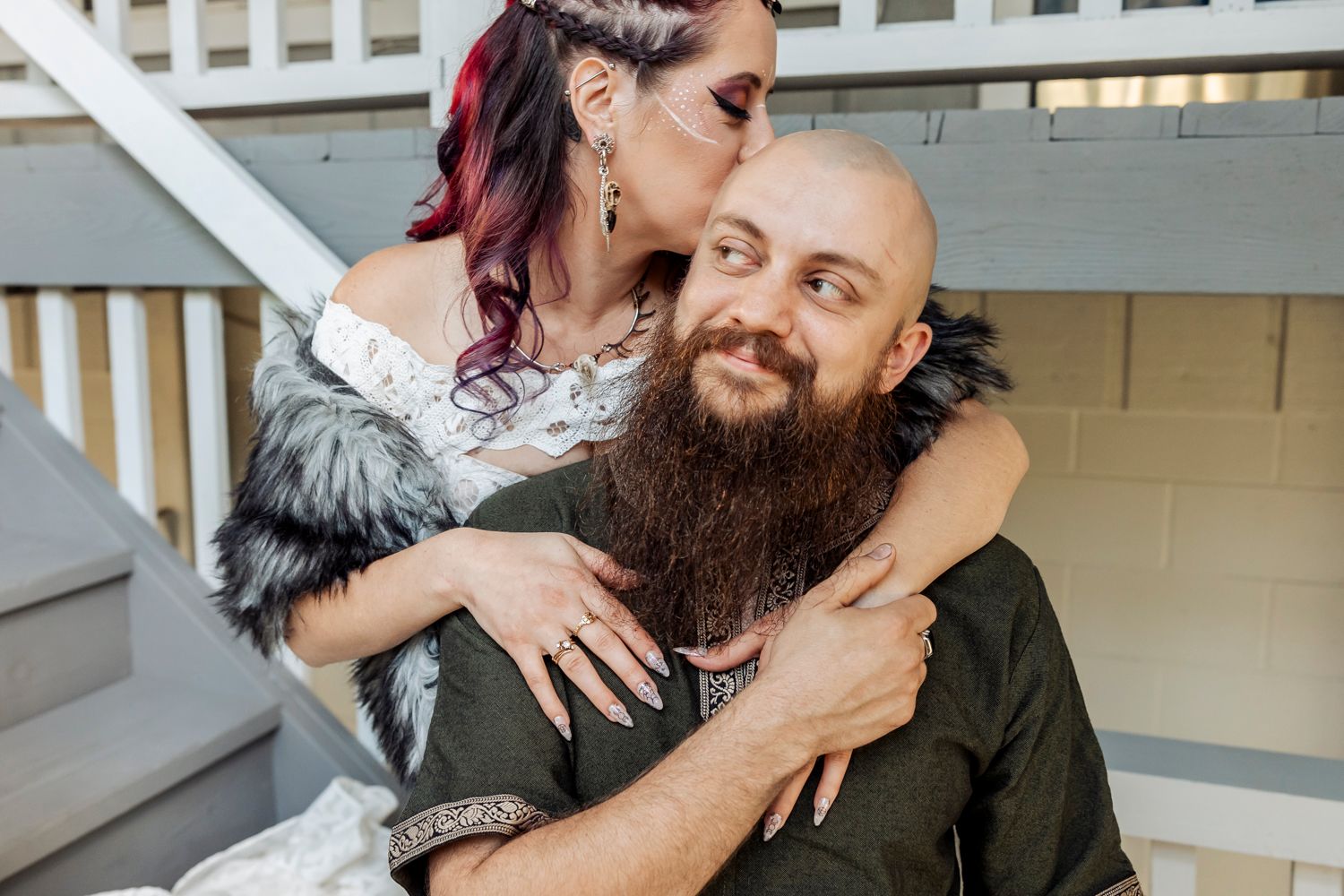 A romantic couple embraces on outdoor stairs with the person wearing a fur wrap and white lace dress.