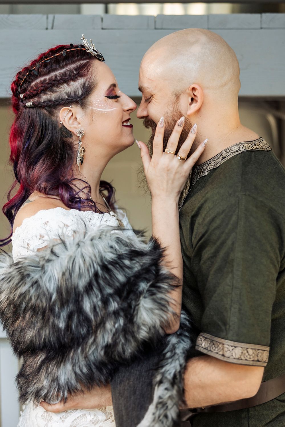 Viking wedding couple with face paint nearly kissing, bride in fur wrap and groom in embroidered green tunic.