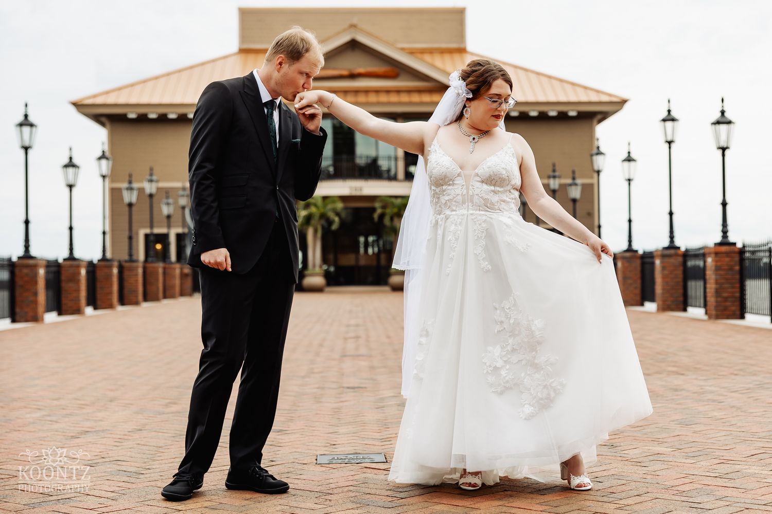 Newlyweds sharing playful moment on brick patio outside Mediterranean-style venue with lamp posts.