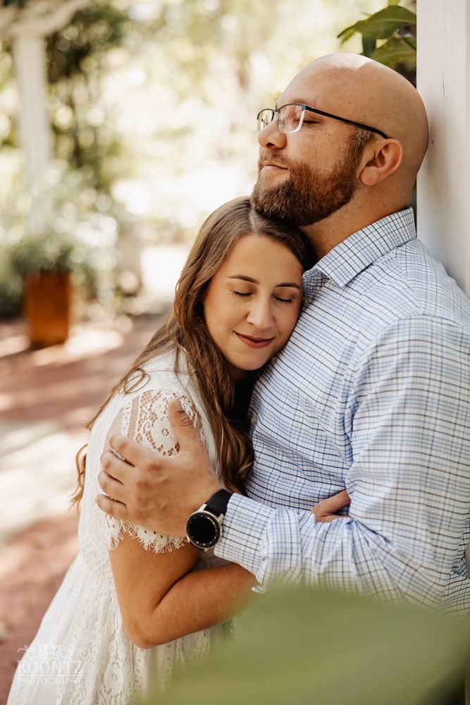 An intimate moment captured between a couple leaning against a white column in warm sunlight.
