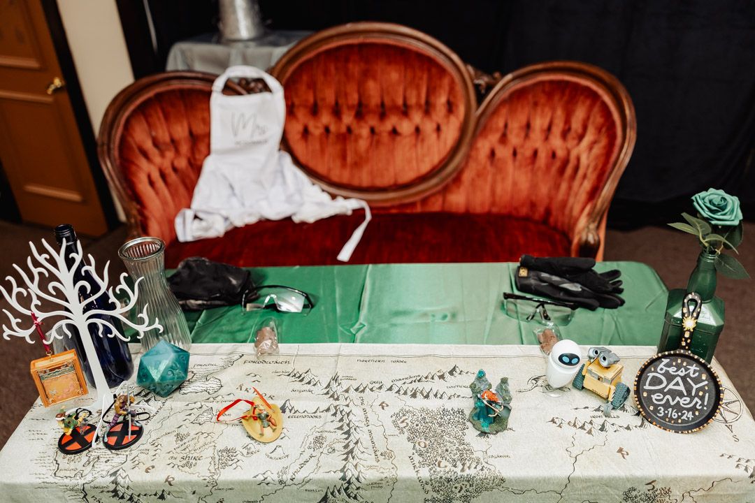 Wedding decorations with greenery and vintage details arranged on white tablecloth with antique sofa.