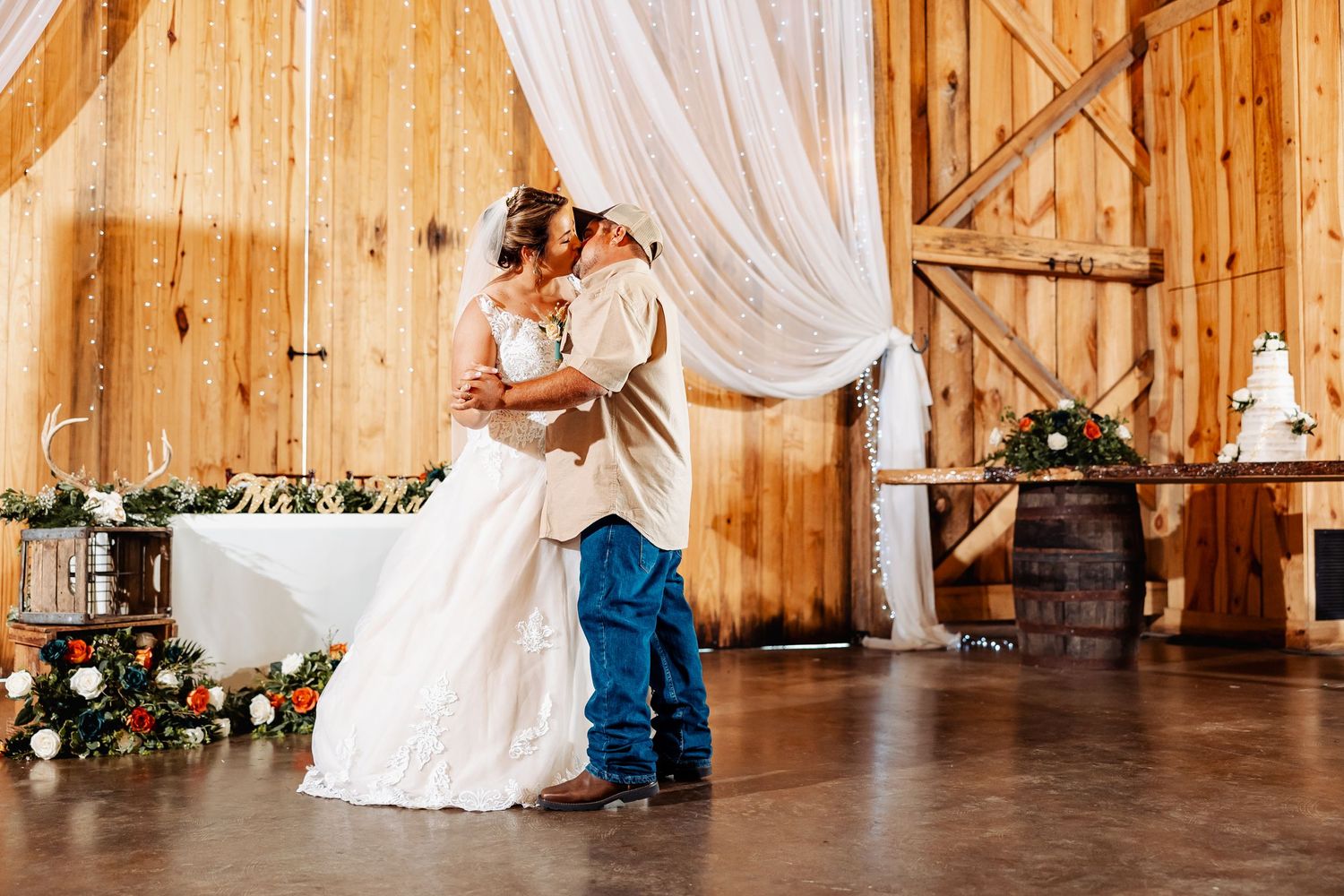 Couple shares romantic first dance in rustic barn wedding venue with wooden walls and flowing white drapery.