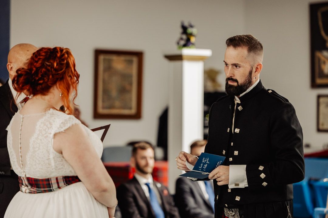 An intimate wedding ceremony moment showing exchange of vows in a room with blue chairs.