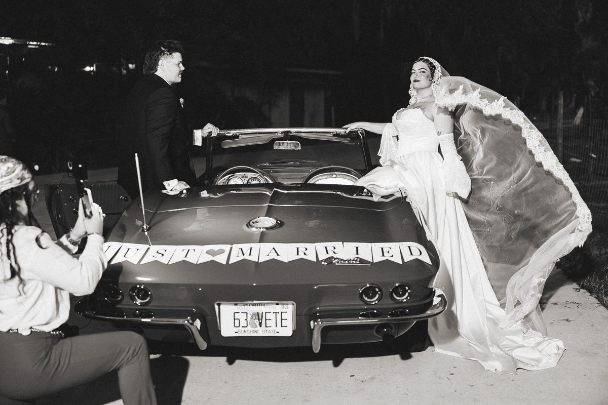 Bride and groom posing beside a classic convertible with Just Married sign at night.