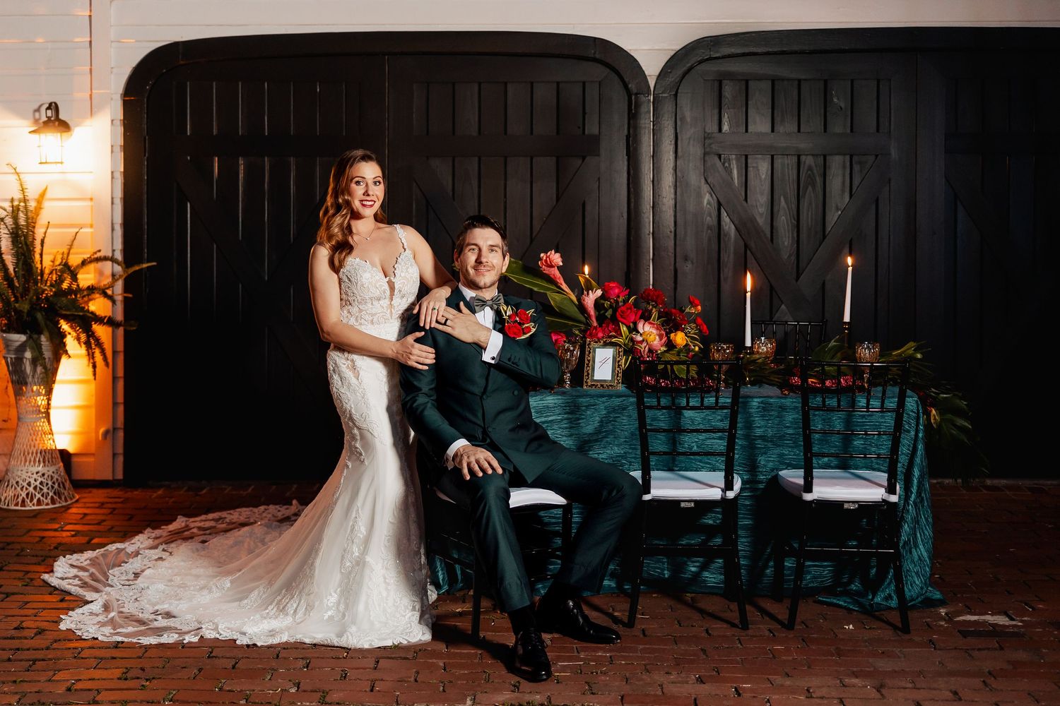 Bride and groom posing elegantly before black doors with floral table decor.