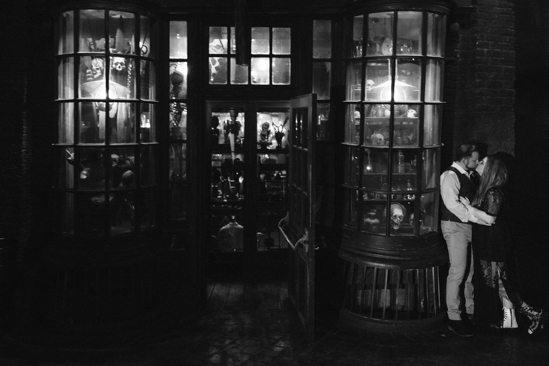 Black and white photo of couple kissing in front of a glowing shop window at night.