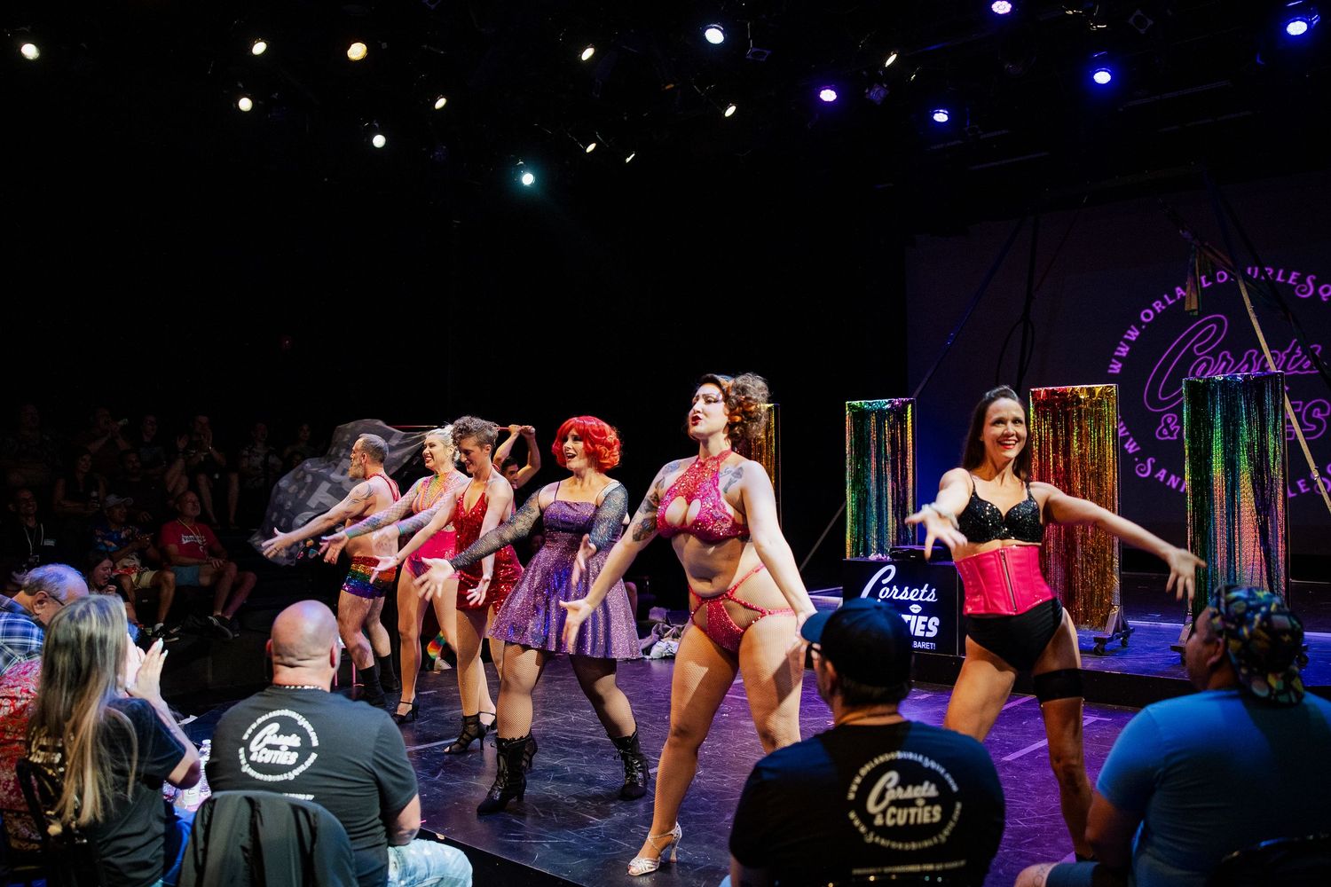 Burlesque performers dancing on stage in lingerie and costumes at a live show with an engaged audience.