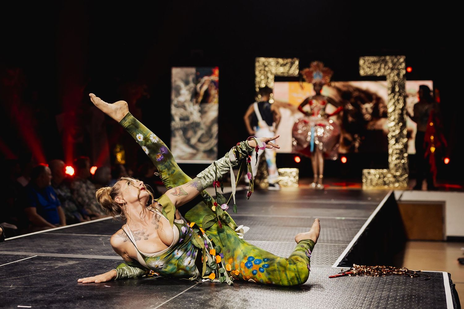 Acrobatic performer in green costume doing a floor pose on a fashion runway.