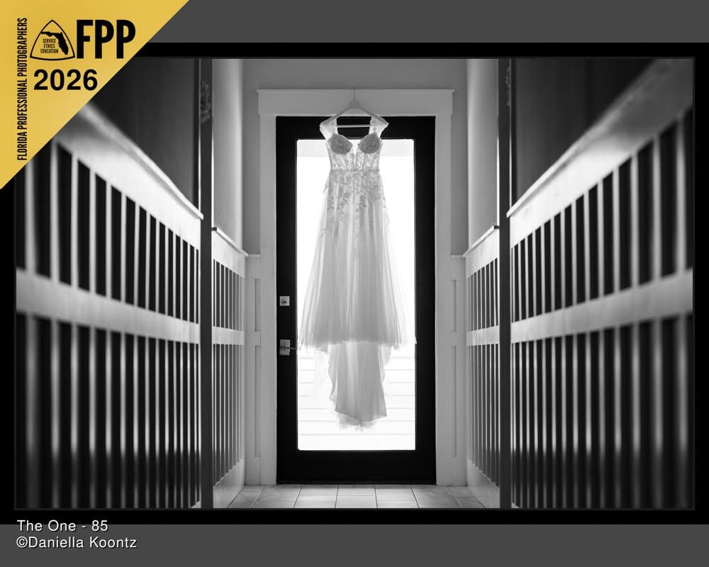 Black and white FPP 2026 award-winning wedding photo of bridal gown hanging in doorway hallway.