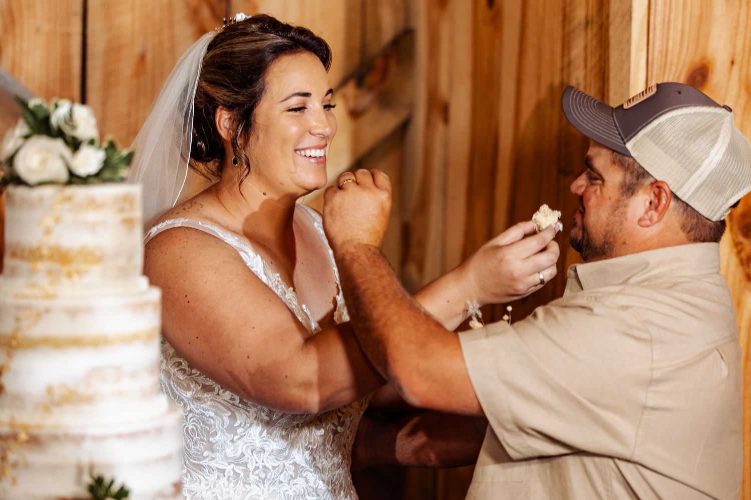 Playful cake-feeding moment between couple at rustic barn wedding reception.