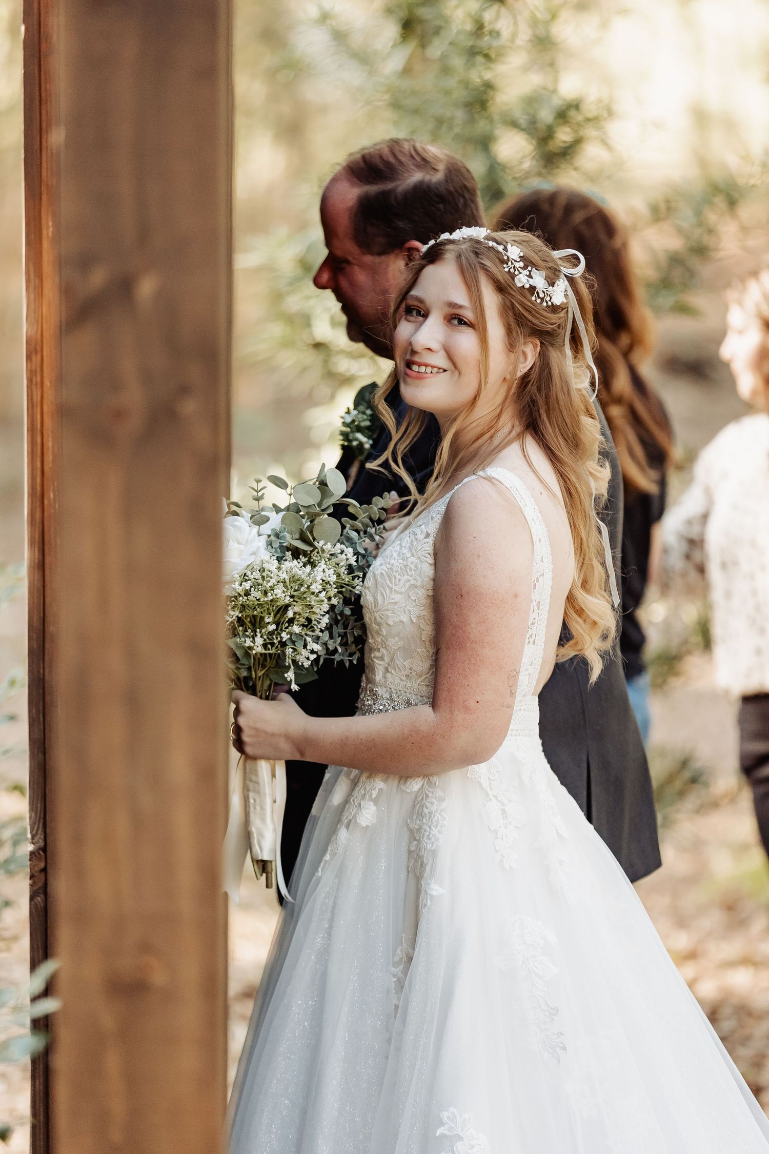 A couple at their rustic outdoor wedding ceremony with the bride wearing a white gown and floral crown.