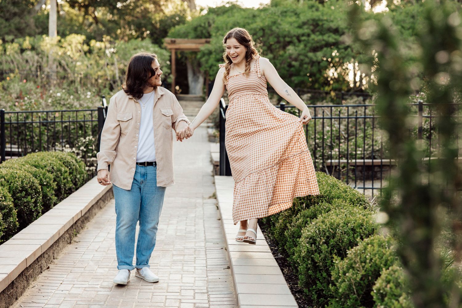 Couple walking along garden path as woman playfully holds dress.