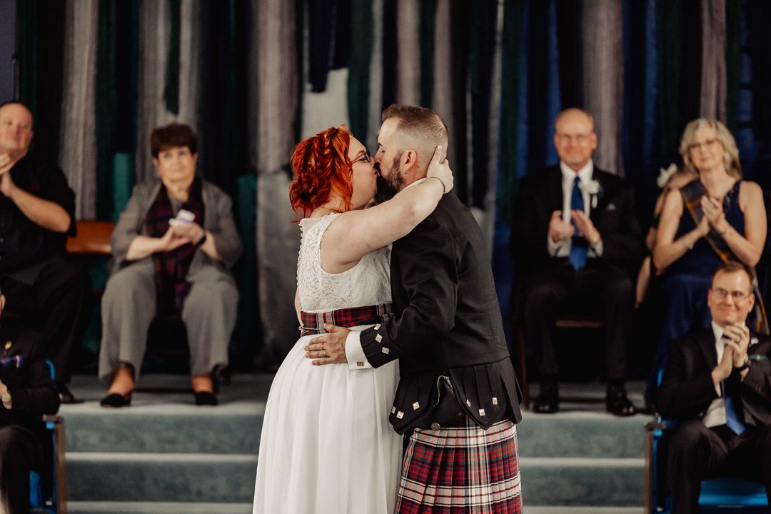 A celebratory moment at a wedding with guests clapping as the couple embraces.