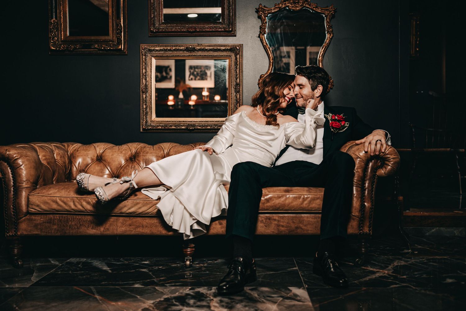 Bride and groom sharing a kiss on a leather couch in moody setting.