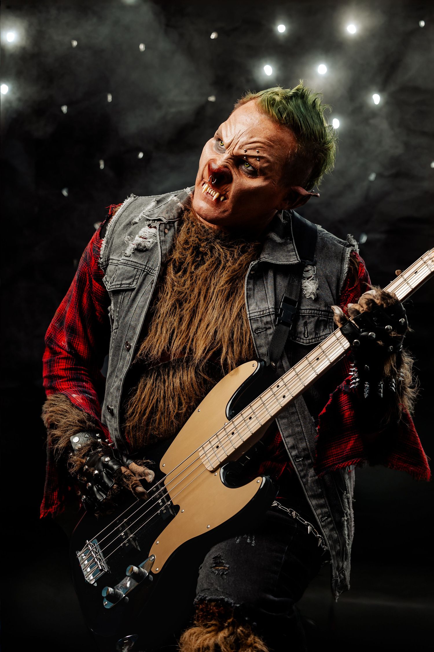 Rock musician in costume playing bass guitar under dramatic stage lighting.