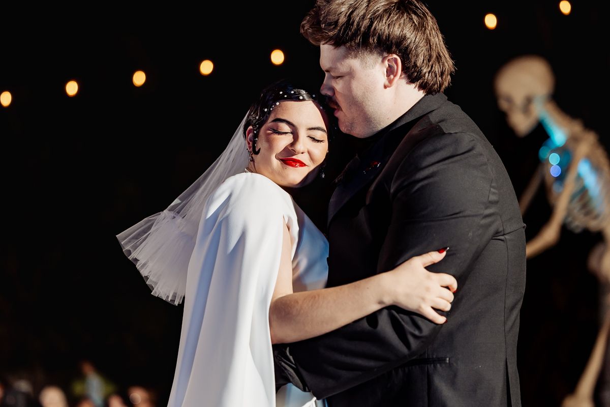 A couple shares a romantic dance together under glowing string lights at an evening celebration.
