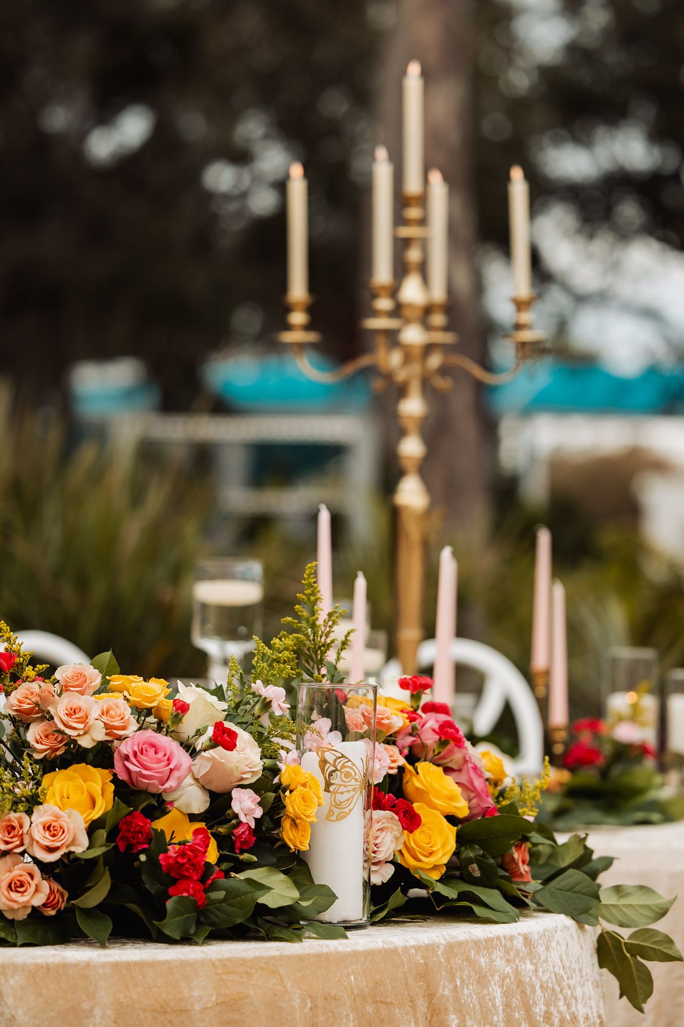Elegant table setting with gold candelabras and colorful floral centerpiece featuring roses in pink, yellow and coral tones.