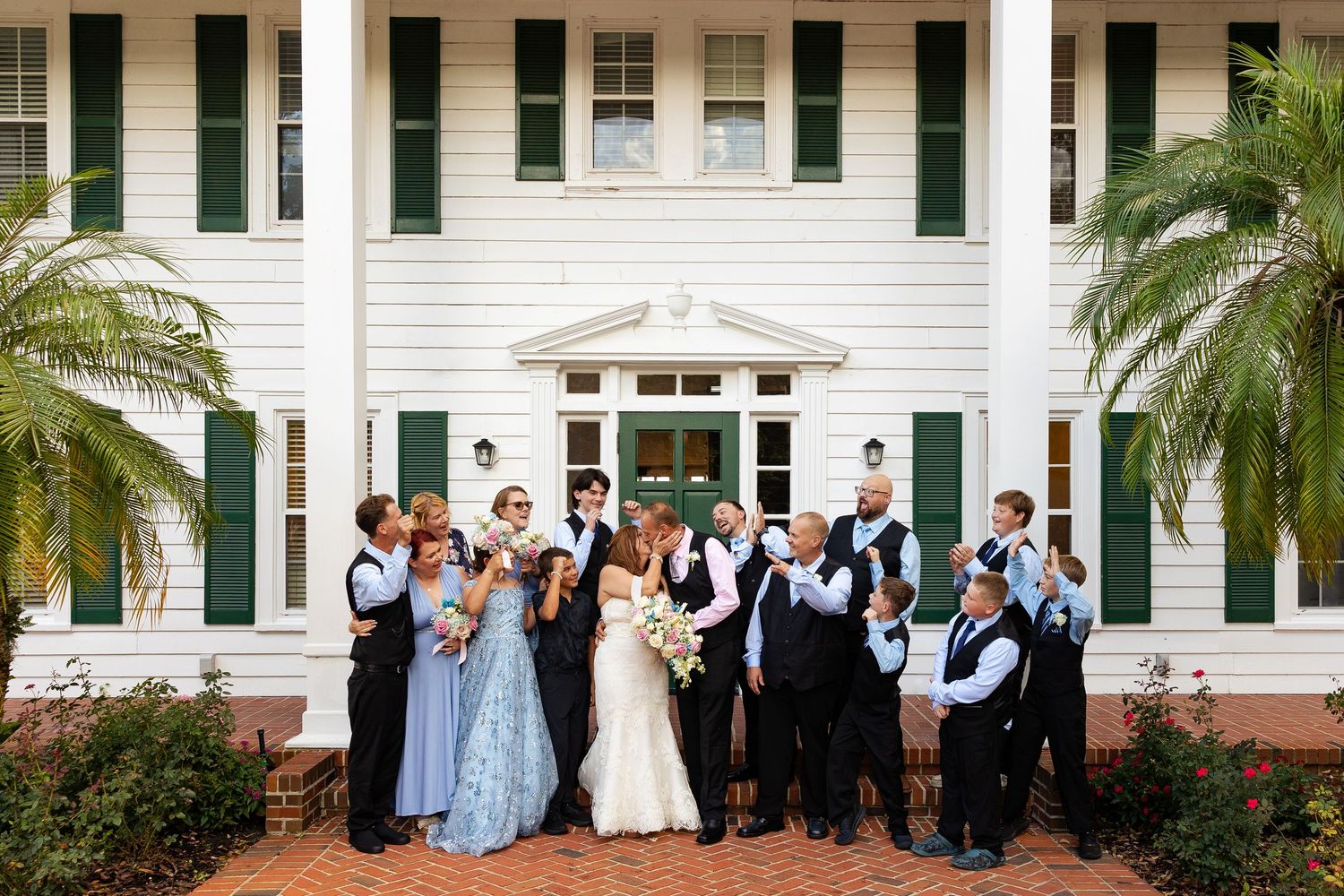 Bride, groom, and wedding party celebrate together outside a classic white Southern estate venue.