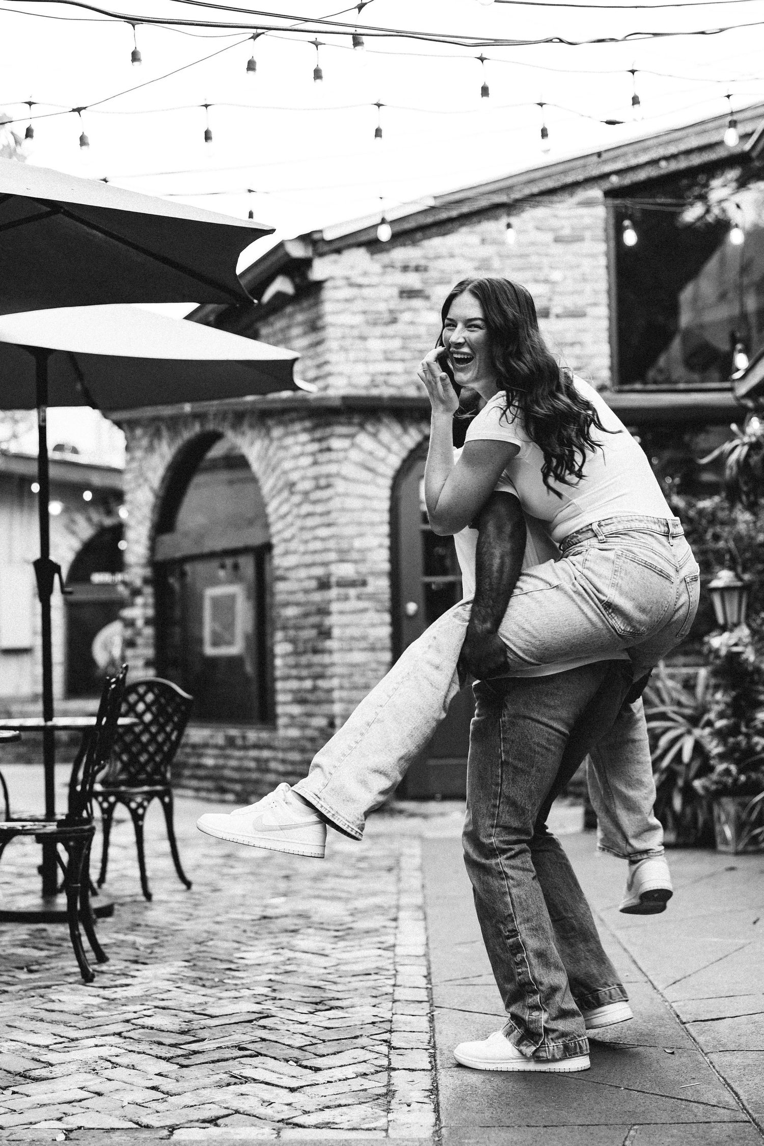 Black and white photo of a laughing woman being carried by her partner outdoors.