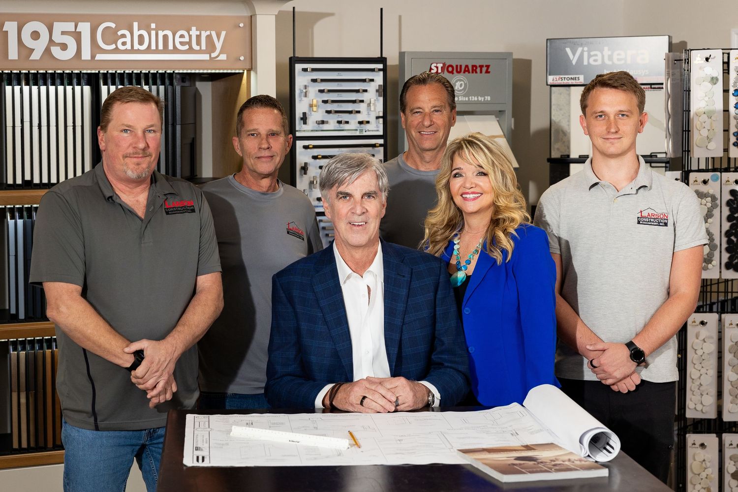 Larson Construction Management team of six posing in a cabinetry showroom with blueprints.