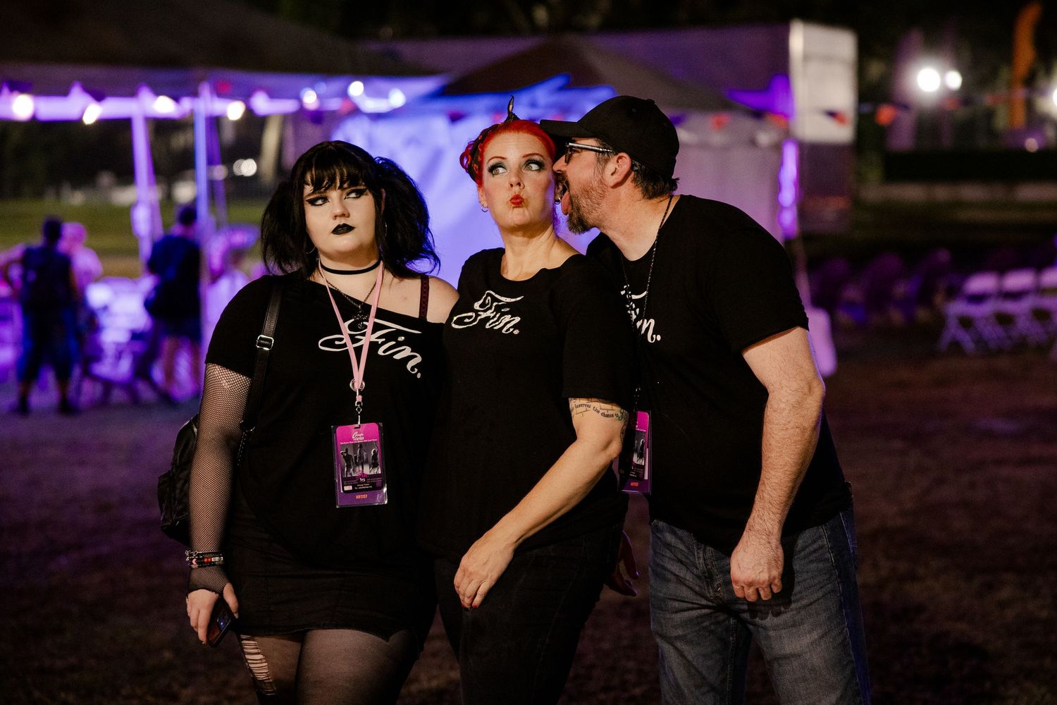 Three people in matching black shirts standing together at an outdoor nighttime music festival.