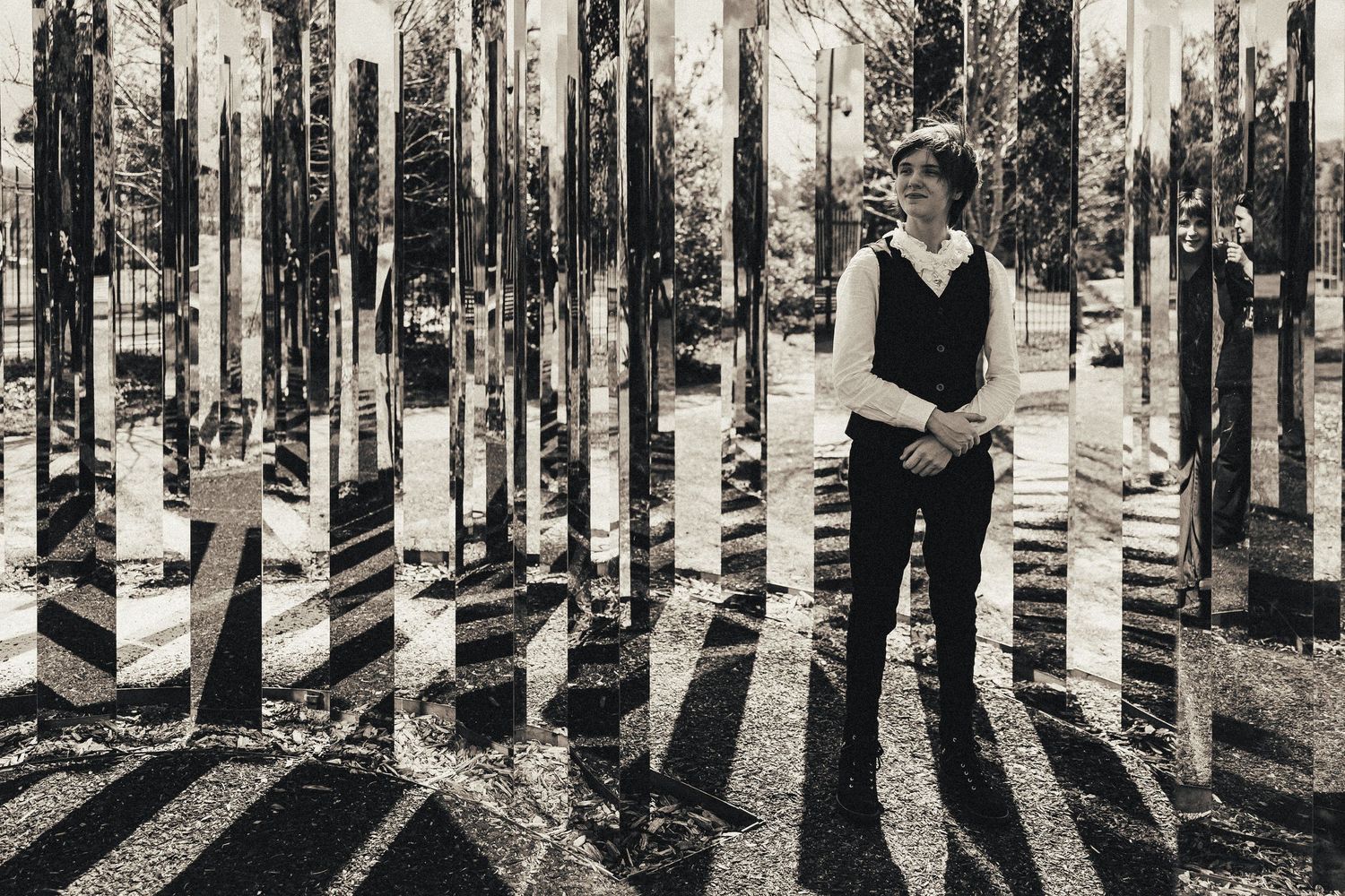 Black and white double exposure portrait of man standing among mirrored columns in a park.