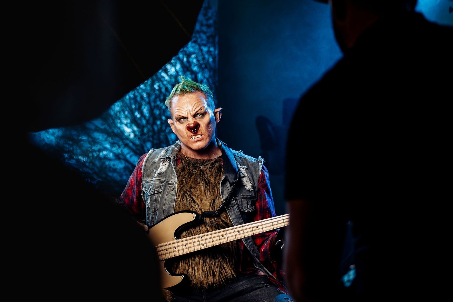 Performer in werewolf costume playing bass guitar under dramatic blue lighting on dark stage.
