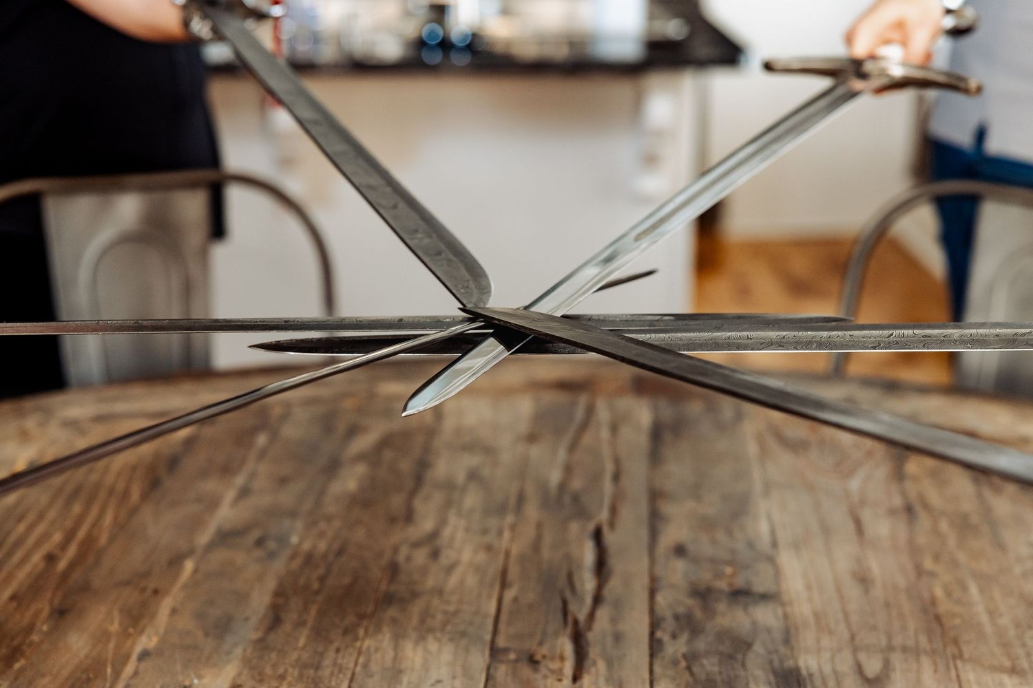 Close-up of multiple medieval sword tips crossing at center point on a rustic wooden table surface.
