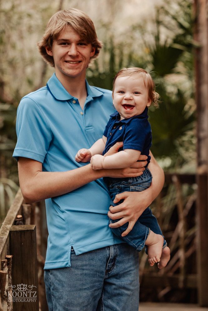 Two people in matching blue polo shirts share a happy moment in front of tropical foliage.