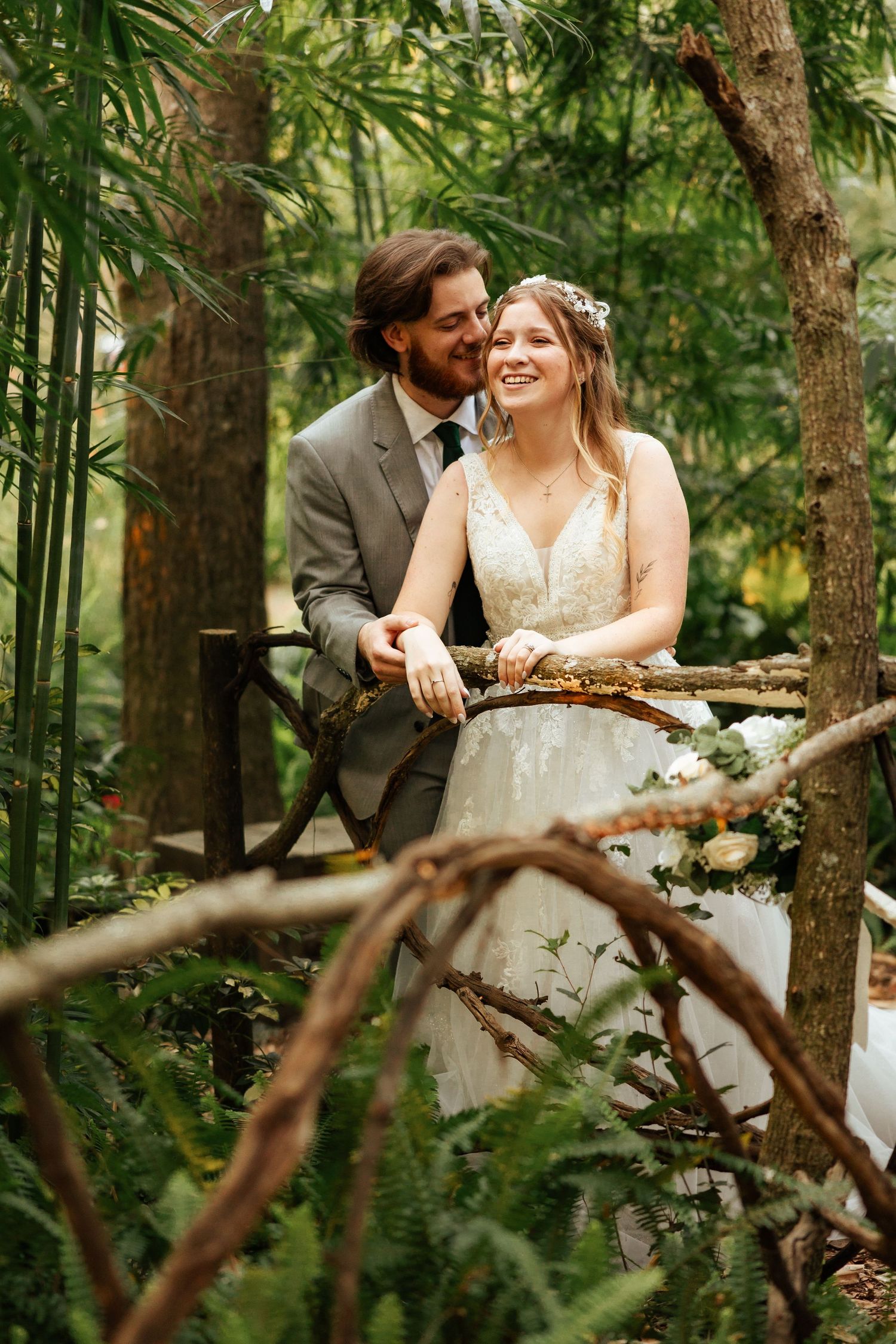 Romantic wedding portrait amidst lush greenery with couple sharing intimate moment on wooden bridge.