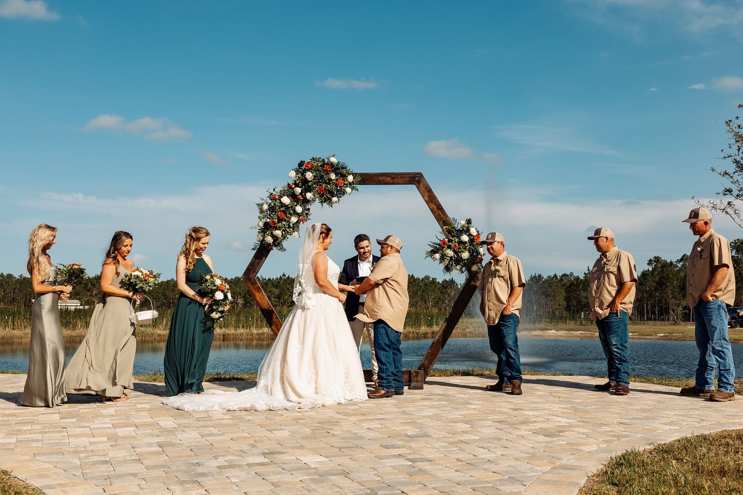 Wedding ceremony under wooden hexagon arch with bridal party overlooking waterfront.