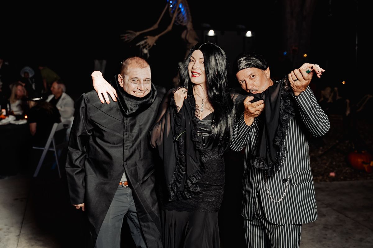 Three wedding guests pose in Halloween costumes resembling the Addams Family at an evening reception.