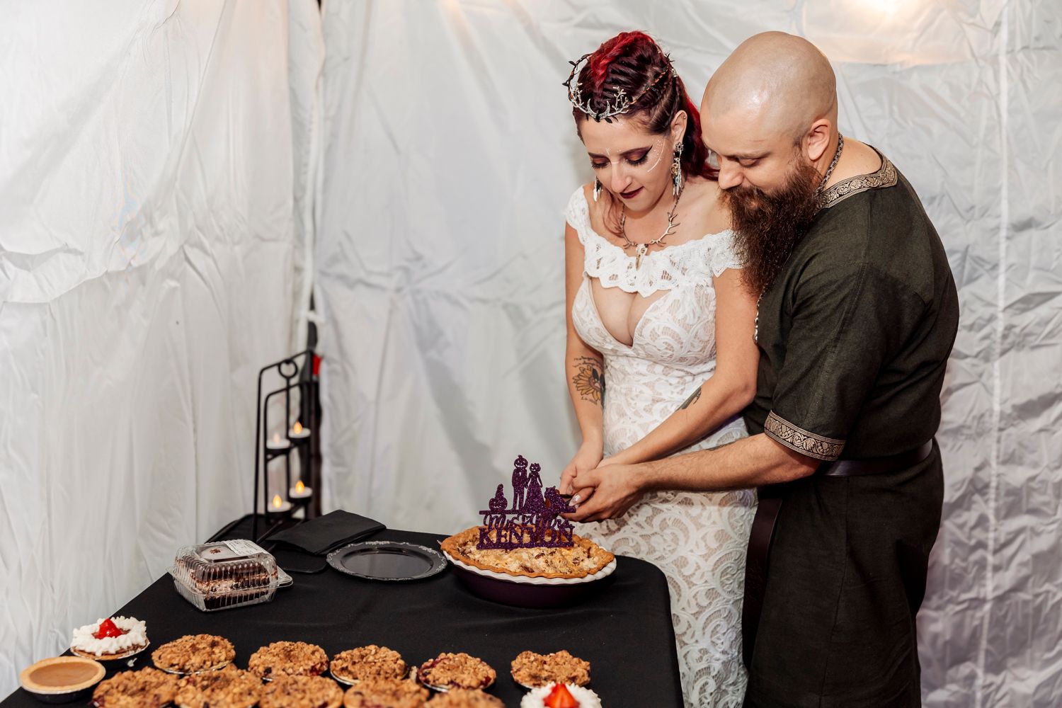 Wedding couple cuts into their dessert together at a reception with treats displayed on black tablecloth.