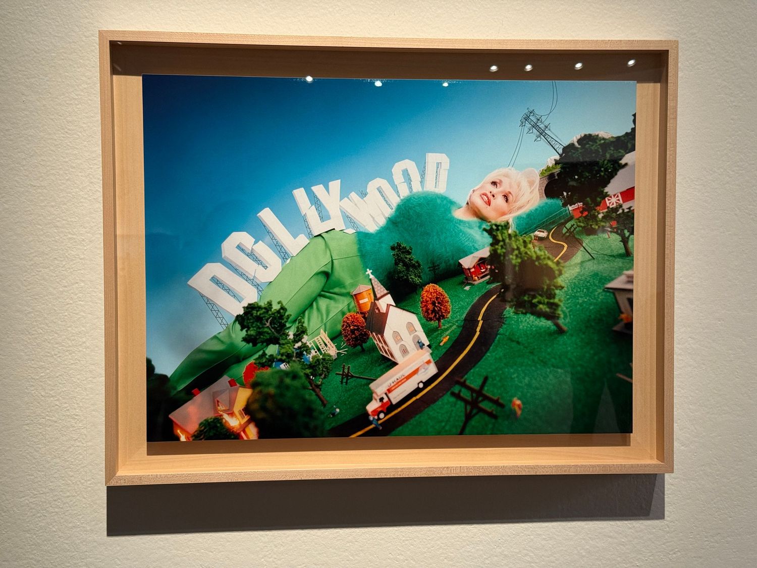 A series of panoramic framed photographs showing green landscapes with curved distortion effects hang on a white wall.