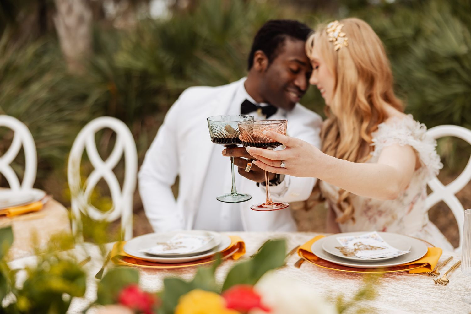 An intimate outdoor dining table set with wine glasses and couples toasting at a romantic garden reception.