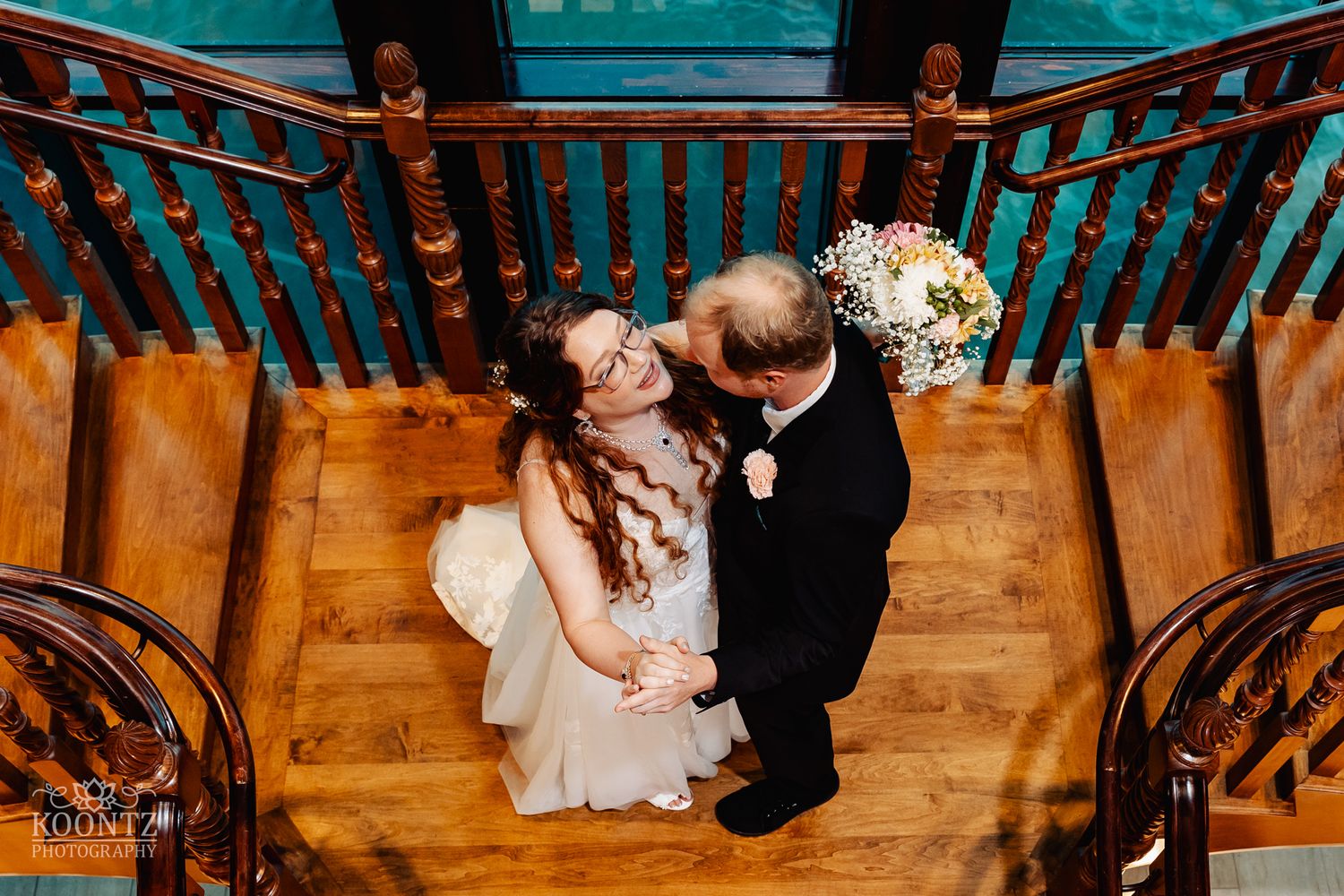 Overhead view of wedding couple sharing intimate moment on wooden spiral staircase.