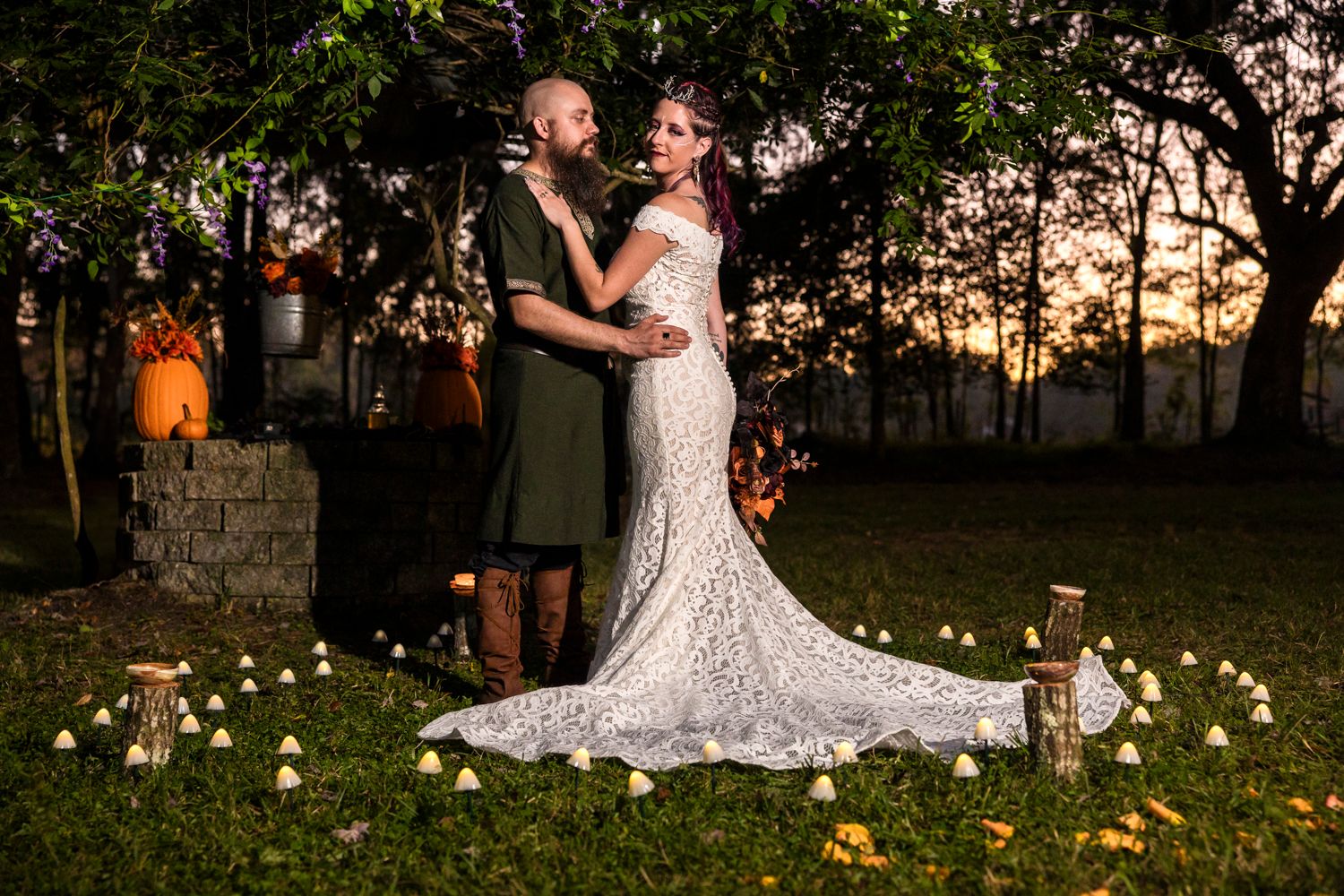 Couple poses in garden setting with twinkling lights and sunset backdrop.
