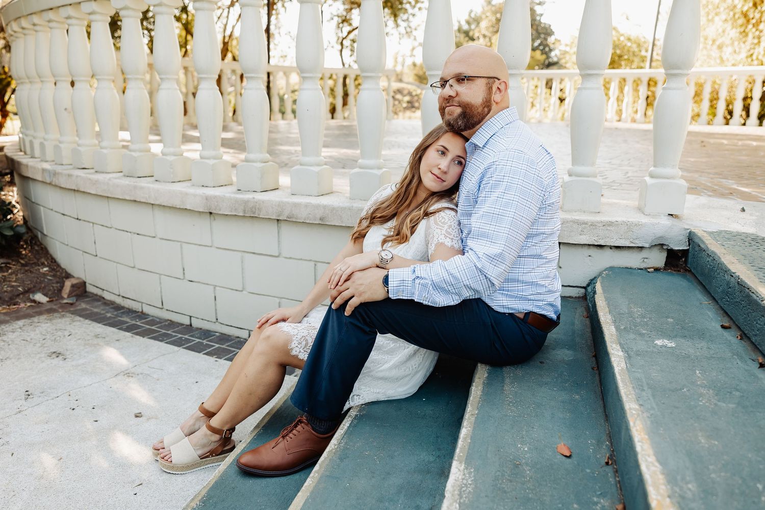 Couple sitting closely together on outdoor steps near white balustrade in warm afternoon light.