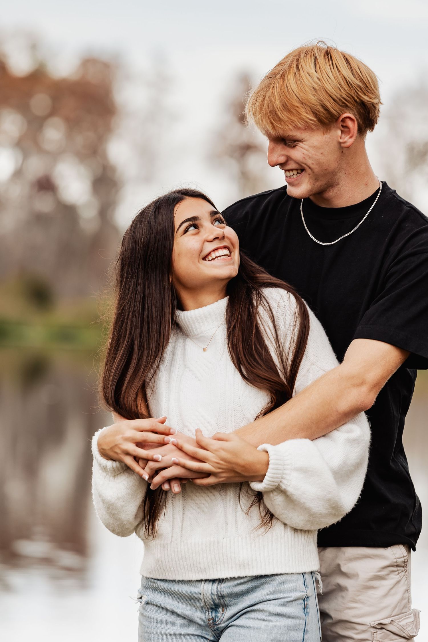 Young couple hugging and gazing at each other lovingly near a reflective lake in autumn.