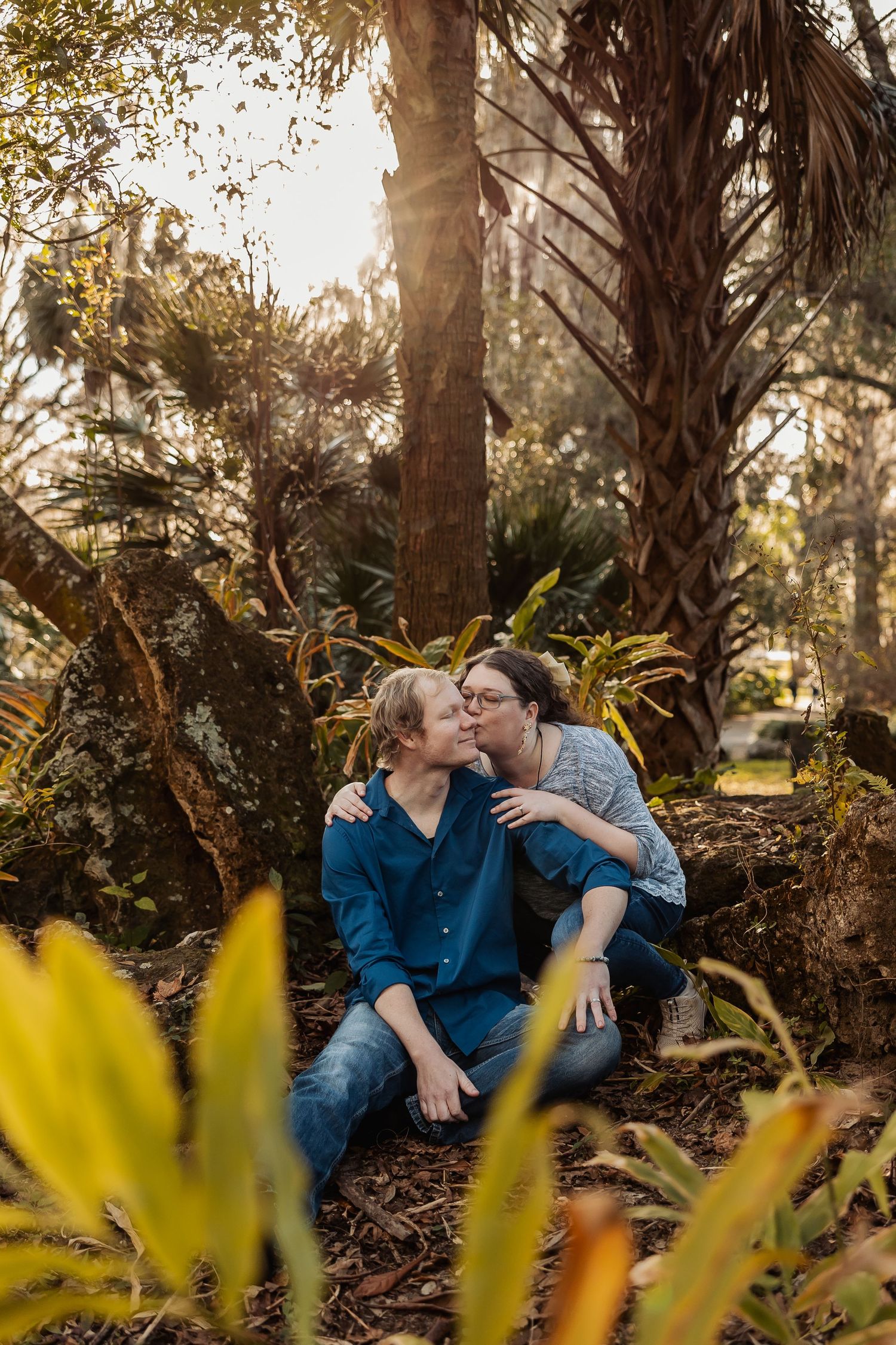 Couple sharing a kiss while sitting together at the base of a tree in a garden.