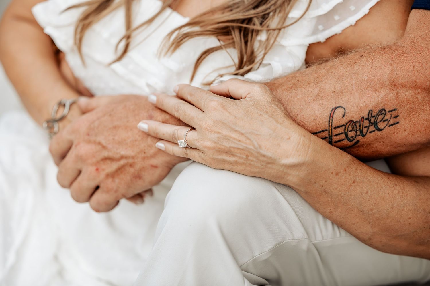 Close-up of couple holding hands showing engagement ring, man with love tattoo on forearm.