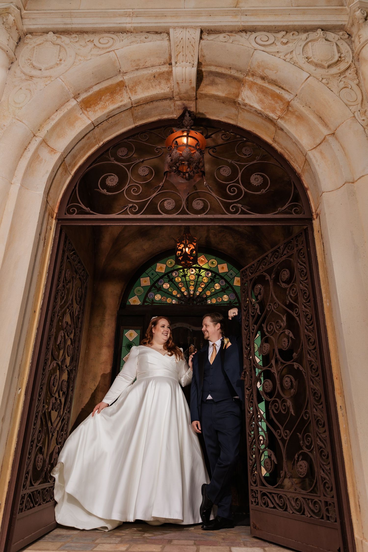 Bride and groom standing in ornate iron doorway of historic venue.