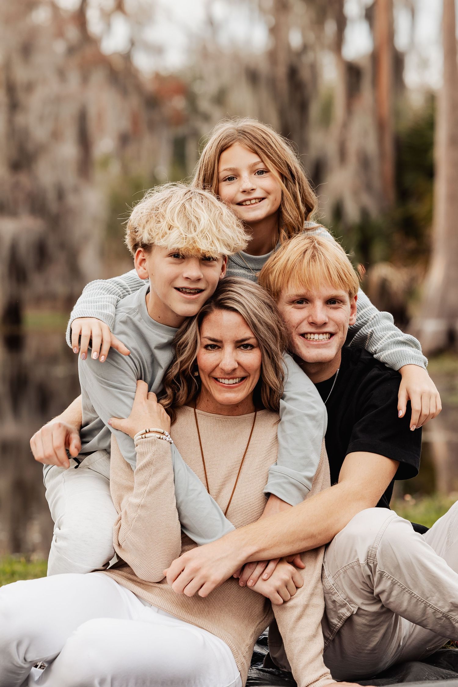 Mother and three children posing in a fun stacked portrait outdoors near a lake.