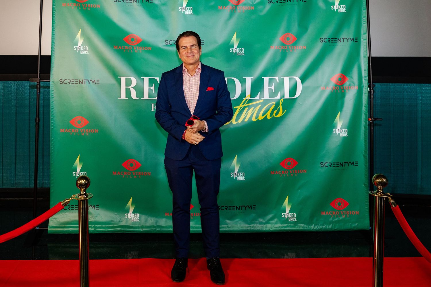 Man in blue suit standing on red carpet at Rekindled for Christmas film premiere event.