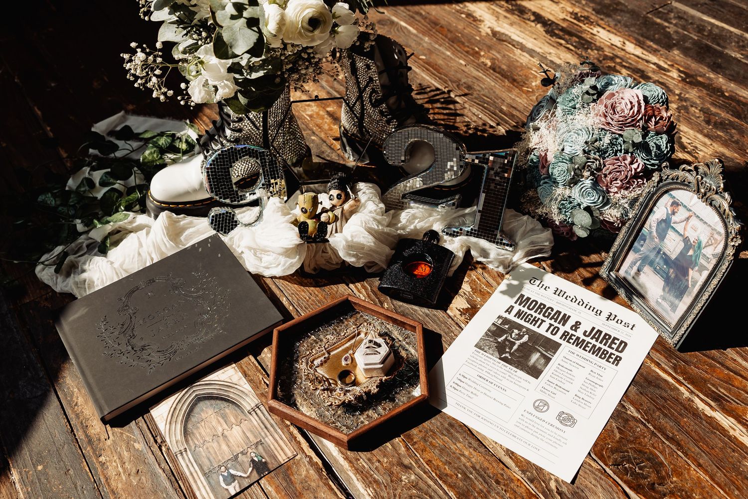 Gothic wedding flat lay with black bouquet, rings, newspaper invitation, and vintage decor on rustic wood.