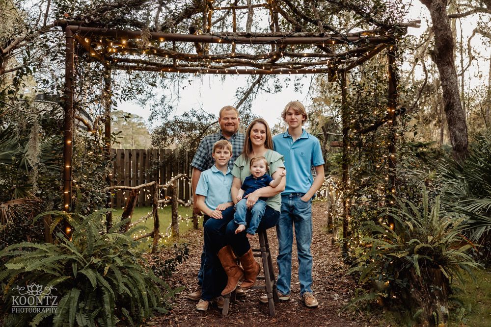 Family portrait under a rustic wooden archway surrounded by lush greenery and natural scenery.