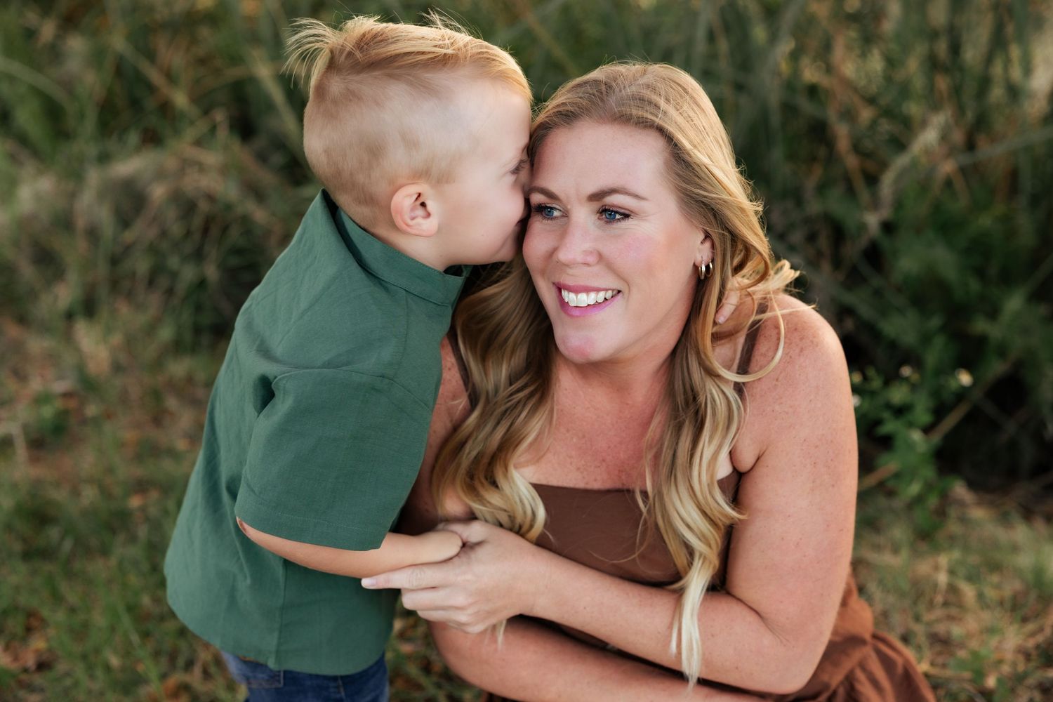 An intimate family moment captured outdoors with golden sunlight filtering through trees in the background.