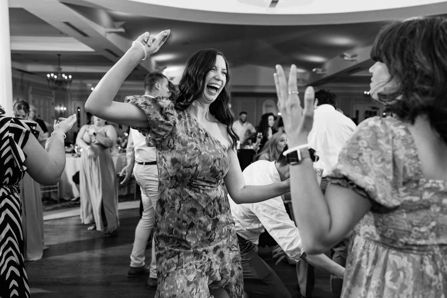 Wedding guest dances joyfully in floral dress during lively black and white reception celebration.